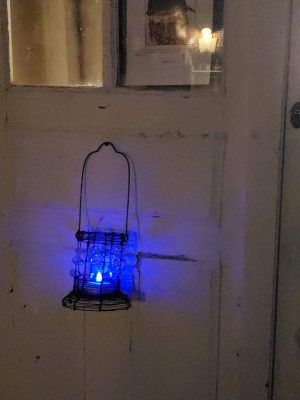 My wire and crystal lantern, with a rainbow shifting LED candle shown in blue phase, and hanging on the weathered white door to my Orquevaux studio 