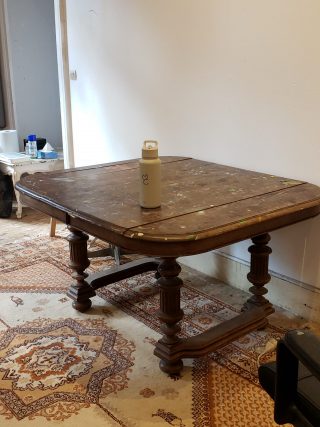 On a floor of plywood and old rugs, an antique carved walnut table is covered with paint splatters. 