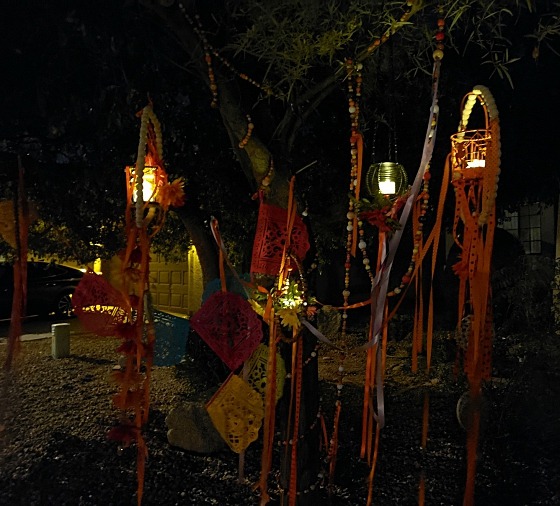 The 2023 Halloween installation at night, the orange silk flowers and ribbons lit by LED lanterns against a backdrop of tree branches and deep blue sky.